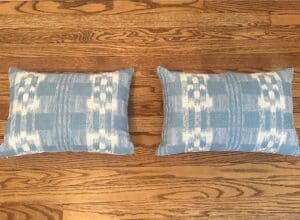 A pair of Sister Parish Mahalo Print Pillows, featuring a blue and white pattern, resting side by side on a wooden floor.