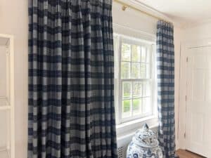 Room with Blue & White Plaid Panels curtains, sunlight streaming through the window, a white door, and a blue-and-white ceramic item in the corner.