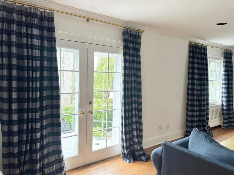 Room with a blue sofa, white walls, wooden floors, and Blue & White Plaid Panels (set of 6), featuring glass doors opening to a garden.