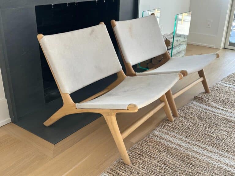 Two modern wooden chairs with light-colored fabric seats sit next to a fireplace on a woven rug.