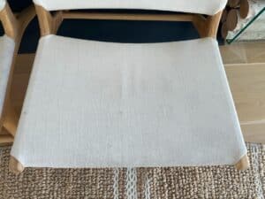A wooden chair with a white fabric seat, positioned on a woven beige rug.