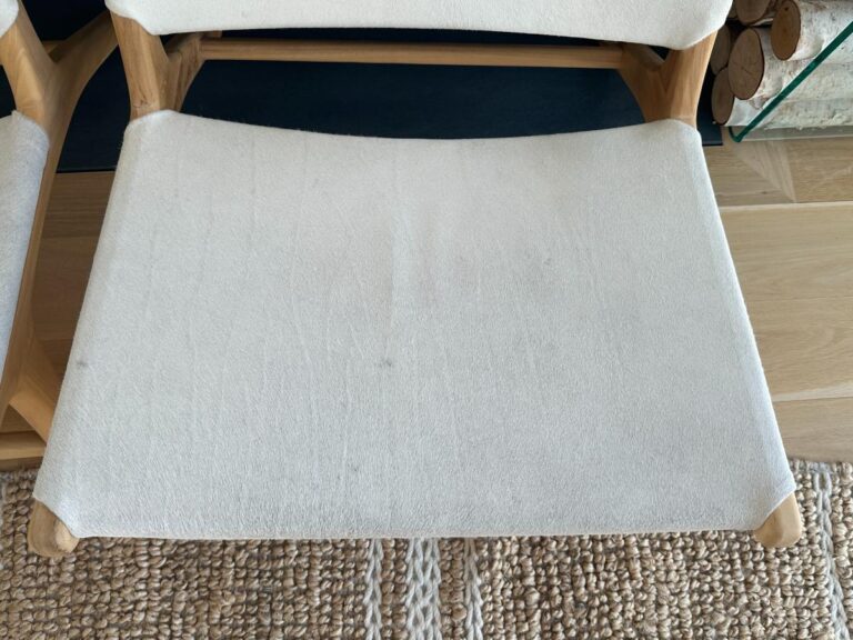A wooden chair with a white fabric seat, positioned on a woven beige rug.