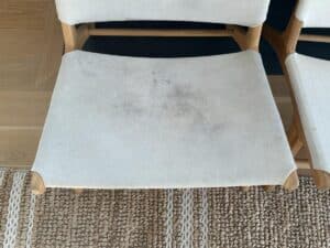 A wooden chair with a stained, off-white fabric seat on a woven rug.