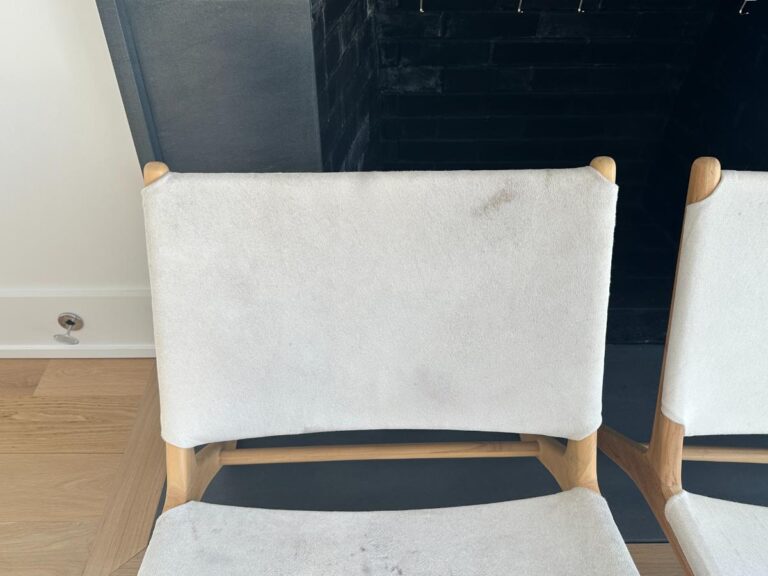 Two light-colored chairs with wooden frames in front of a black fireplace and a white wall.
