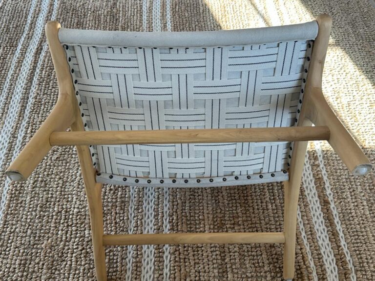A wooden chair with a woven fabric backrest sits on a textured, patterned rug.