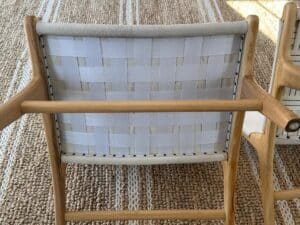 A wooden chair with a white woven fabric backrest on a textured beige rug with white stripes.