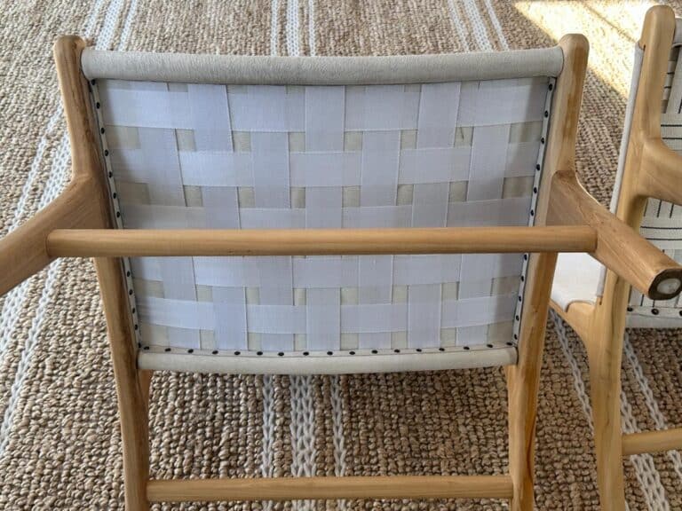 A wooden chair with a white woven fabric backrest on a textured beige rug with white stripes.