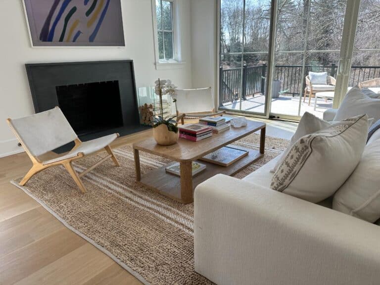 Bright living room with modern furniture, a wooden coffee table, and large windows overlooking a deck and trees.