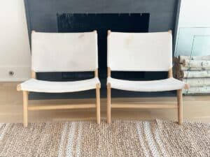 Two white canvas chairs with wooden frames are placed side by side in front of a fireplace.