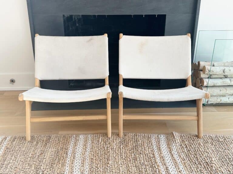 Two white canvas chairs with wooden frames are placed side by side in front of a fireplace.