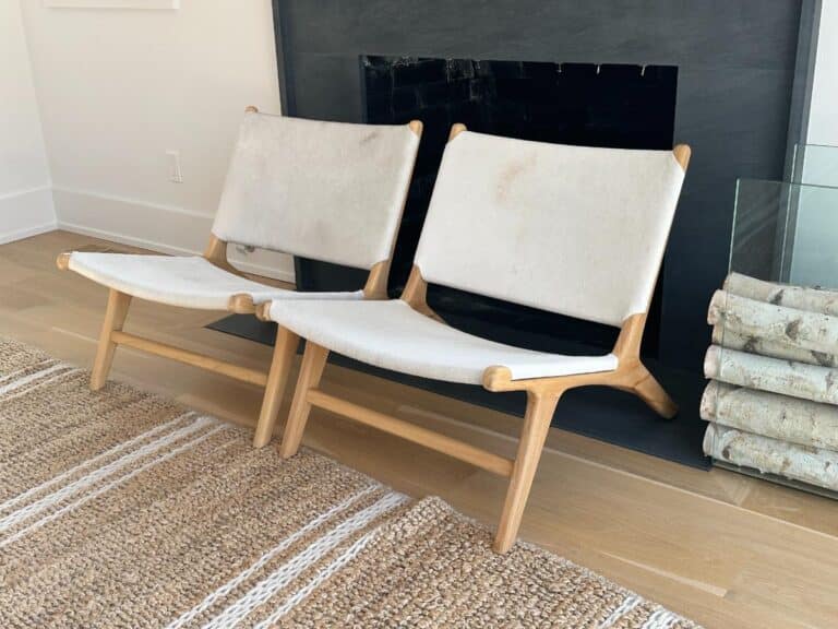 Two modern wooden chairs with white fabric seats are placed side by side in front of a fireplace.