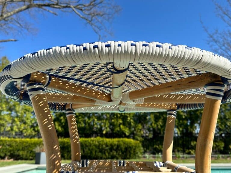 Close-up of a woven table top from below with blue sky and trees in the background.