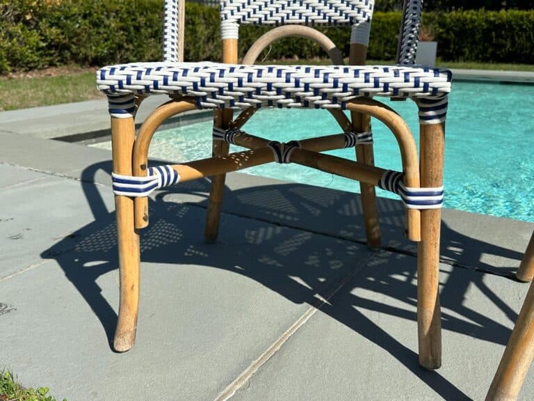 A woven rattan chair casting a shadow on poolside tiles, with clear pool water in the background.