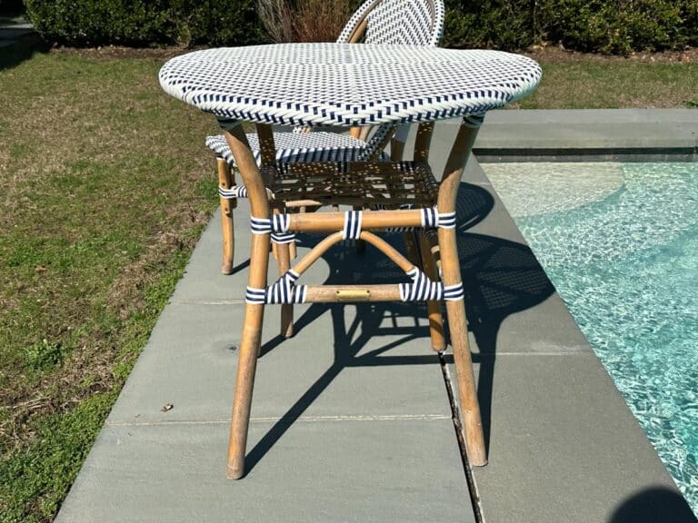Wicker table and chairs with blue-striped pattern on patio beside a pool.