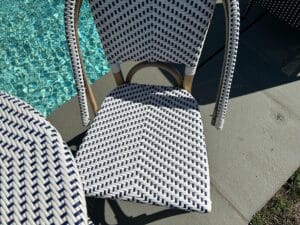 Woven chair by a pool on a sunny day, casting shadows on the poolside pavement.