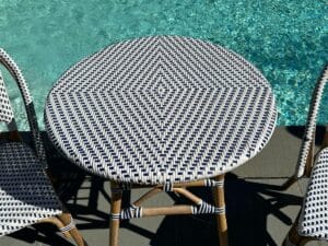 Round wicker table by a pool, casting shadows in the sunlight.