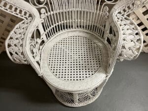 A Vintage Hollywood Regency Style Peacock Chair features intricate wicker weaving and a circular seat, set on a gray floor.