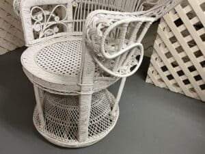 A Vintage Hollywood Regency Style Peacock Chair with intricate woven patterns and decorative armrest detail sits on a gray floor.