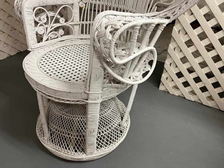 A Vintage Hollywood Regency Style Peacock Chair with intricate woven patterns and decorative armrest detail sits on a gray floor.