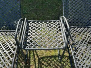 Five black metal chairs with latticed backs and seats arranged in a circular pattern on grass.
