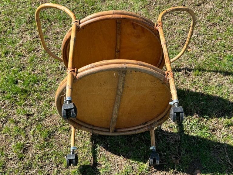 Two wooden chairs stacked upside down on grass, with visible metal wheels and handles.