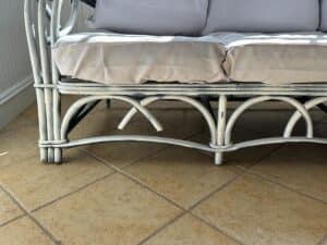 White wicker loveseat with gray cushions on a tiled floor.