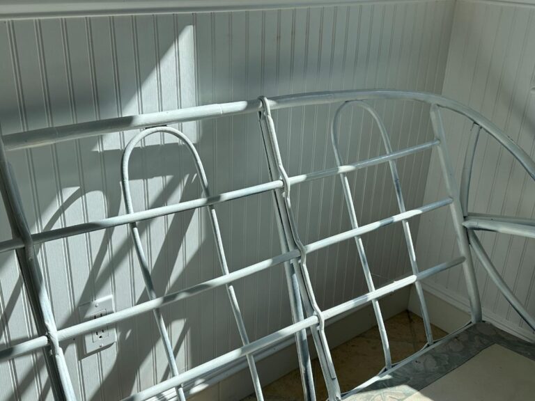 Two vintage metal headboards leaning against a paneled wall, with sunlight casting shadows.