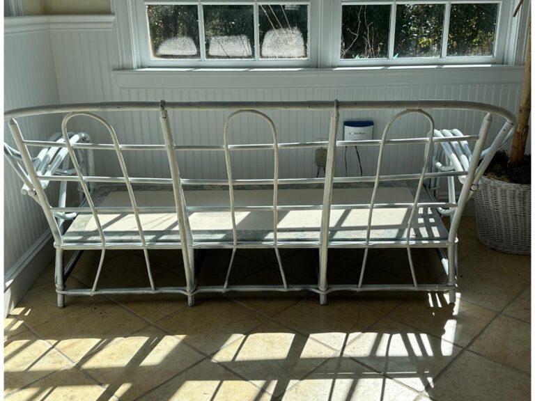 Metal-framed bench with a missing cushion in a sunlit room, on a tiled floor with a potted plant beside it.