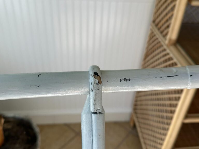 Close-up of a worn, chipped metal joint in a painted structure, with wicker shelves blurred in the background.