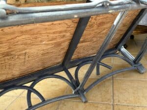 A wrought iron table with a wooden top is turned upside down on a tiled floor.