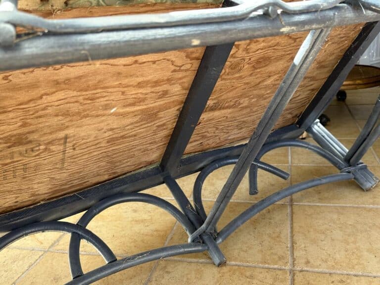 A wrought iron table with a wooden top is turned upside down on a tiled floor.