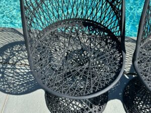 Woven metal chair casting intricate shadows beside a sparkling blue pool.