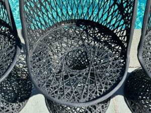 Woven black chair with an intricate spiral design beside a swimming pool.