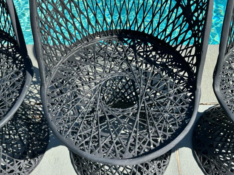Woven black chair with an intricate spiral design beside a swimming pool.