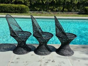 Three black wicker chairs by a poolside with sunlit reflections on the water.