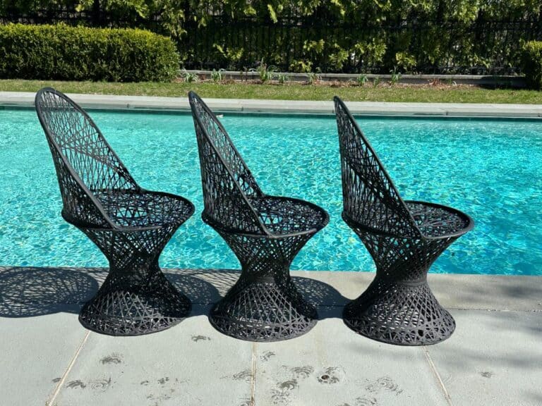 Three black wicker chairs by a poolside with sunlit reflections on the water.