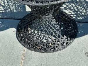 A black wire mesh table casting intricate shadows on a gray stone surface under sunlight.