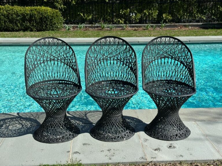 Three black woven chairs by a blue swimming pool on a sunny day.