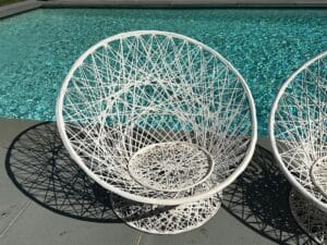 A white woven chair by a turquoise pool on a sunny day.