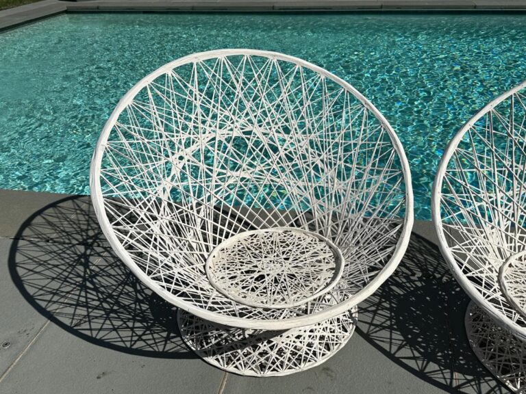 A white woven chair by a turquoise pool on a sunny day.