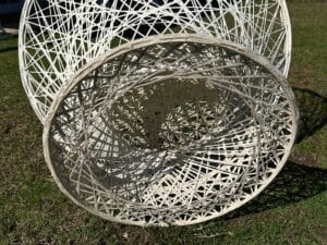 Woven circular sculpture with intricate patterns, placed on grass, casting shadows.