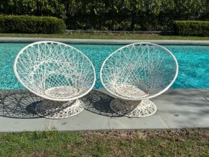 Two white wicker chairs by a pool, casting intricate shadows on the gray stone poolside.