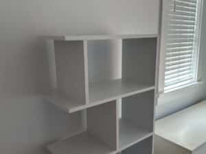 White cube shelving unit beside a window with closed blinds in a bright room.