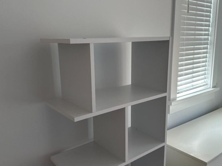 White cube shelving unit beside a window with closed blinds in a bright room.