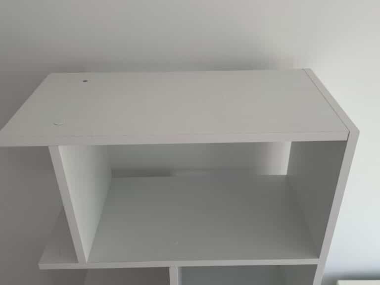 A white, empty shelf unit against a plain white wall, viewed from an angle above.