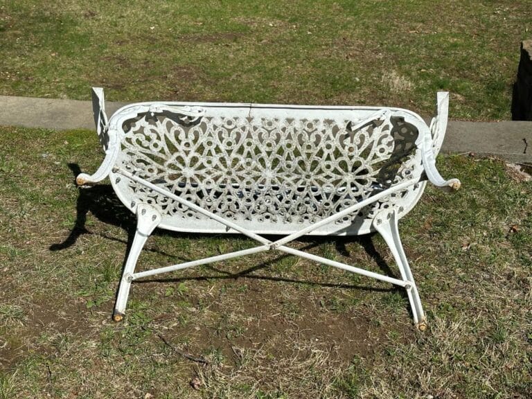 White decorative metal bench flipped upside down on grass near a concrete path.