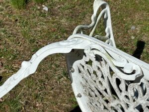 Close-up of a white, ornate metal garden chair with intricate patterns on a grassy surface.