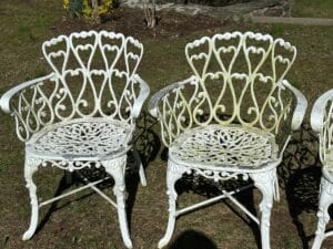 Two ornate white metal chairs with heart-shaped designs on a grassy area.