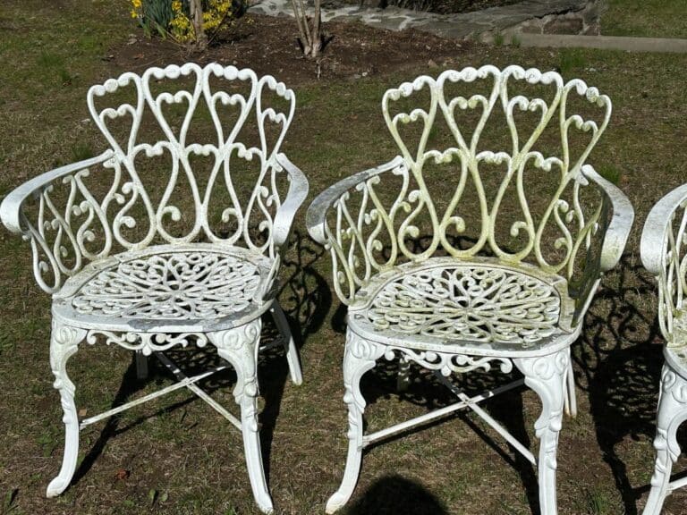 Two ornate white metal chairs with heart-shaped designs on a grassy area.