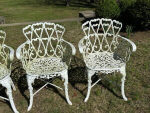 Two white ornate metal chairs on grass with heart-shaped backrests.